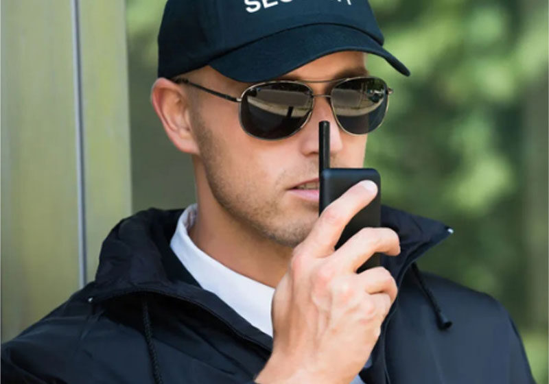 Security guard using a walkie-talkie outdoors.